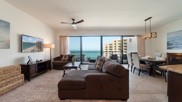 Ein modernes Wohnzimmer mit großem Fenster zum Meer, einem Deckenventilator und einem Essbereich mit Blick.