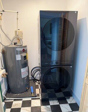 A water heater and a large, modern, metallic unit, possibly a water tank or boiler, in a room with checkered flooring. - Wild Finch Stay - Sauna • Cold Plunge • Hot Tub (Colorado Springs)