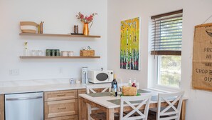 A kitchen with a dishwasher, wooden cabinets, a microwave, and a dining table with chairs. - Wild Finch Stay - Sauna • Cold Plunge • Hot Tub (Colorado Springs)