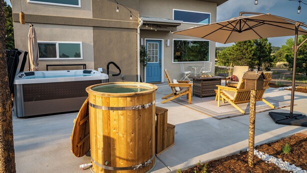 A spa area with a hot tub, wooden barrel, outdoor seating, and a covered patio. - Wild Finch Stay - Sauna • Cold Plunge • Hot Tub (Colorado Springs)