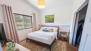 A bedroom with a bed, a desk, a chair, a window with curtains, and a painting on the wall. - Wild Finch Stay - Sauna • Cold Plunge • Hot Tub (Colorado Springs)