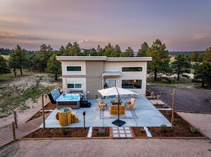 Una casa moderna de dos pisos con jacuzzi, mobiliario exterior y vistas del paisaje circundante.