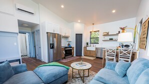 A modern living room with a sofa, a coffee table, and a kitchen area with a refrigerator and stove. - Wild Finch Stay - Sauna • Cold Plunge • Hot Tub (Colorado Springs)