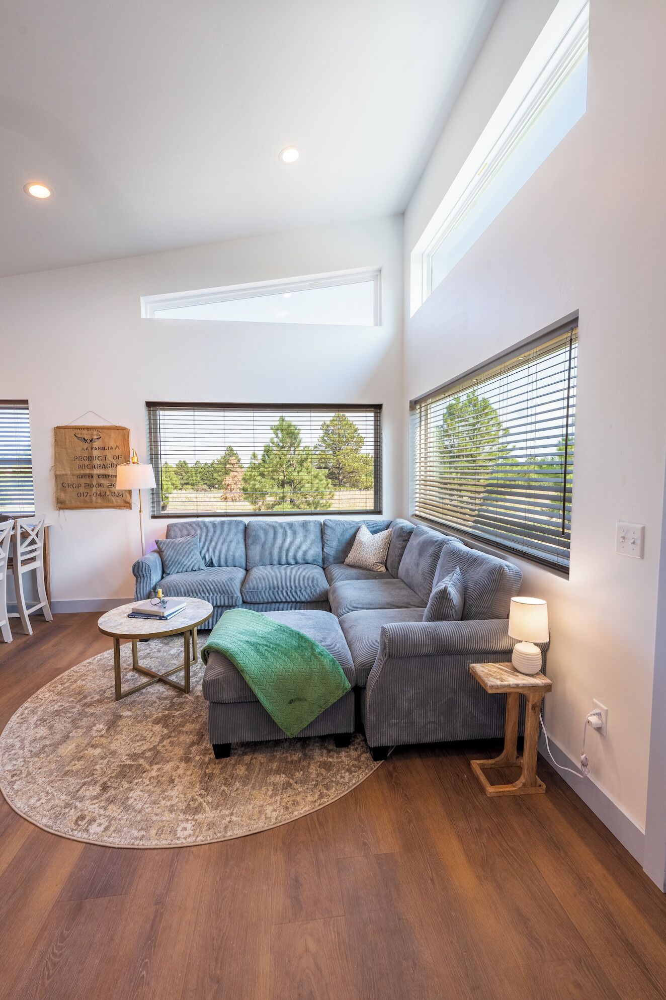 A modern living room with a sectional sofa, a round coffee table, and a large window with blinds.