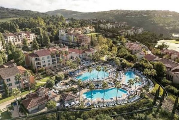 Un complexe hôtelier doté de plusieurs piscines, entouré d’une végétation luxuriante et de bâtiments résidentiels.