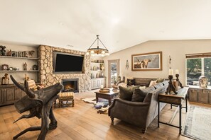 Ein geräumiges Wohnzimmer mit Kamin aus Naturstein, einem großen Flachbildfernseher und einer gemütlichen Sitzecke mit Sofa und Sesseln.