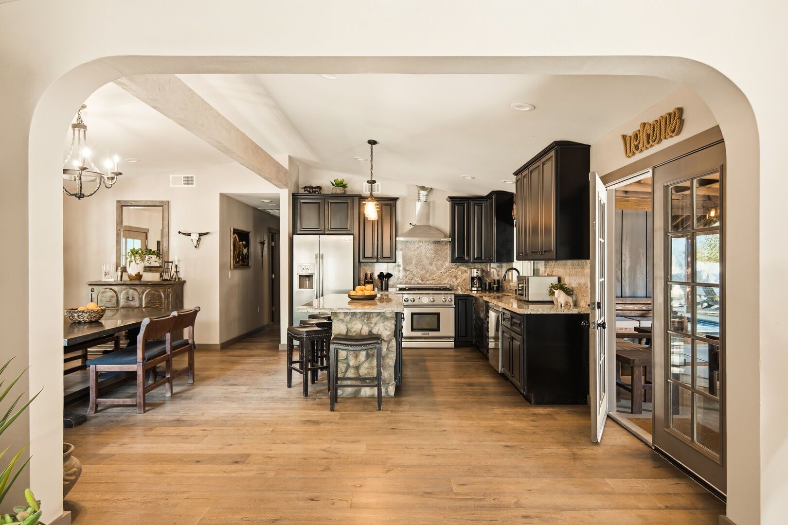 A modern kitchen with dark cabinets, a central island, and a dining area with a wooden table and chairs.