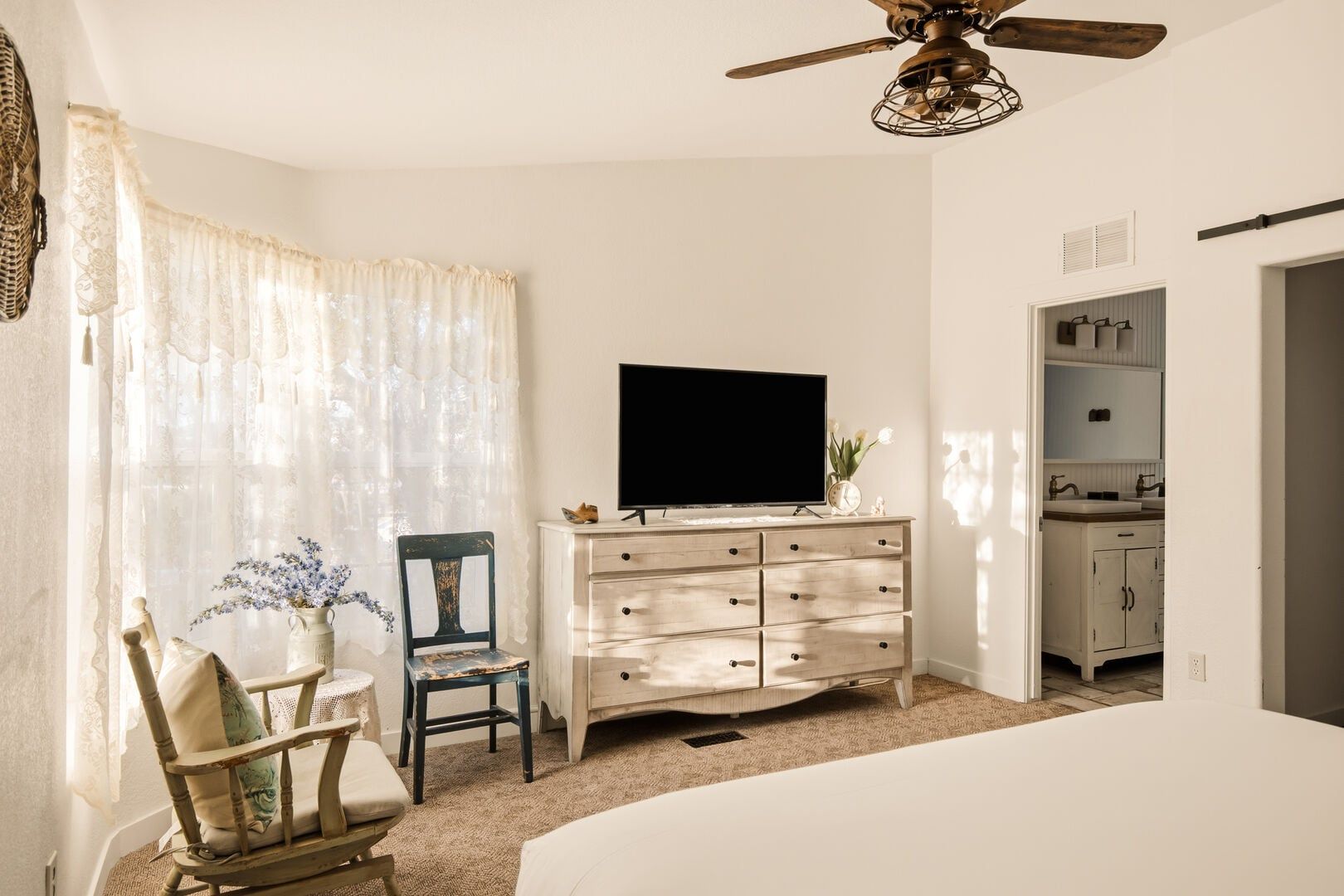A bedroom with a bed, a dresser, a chair, a television, and a ceiling fan.