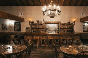 Eine Bar mit Holzhockern, einem Kronleuchter und einer Wandvitrine für Spirituosen.