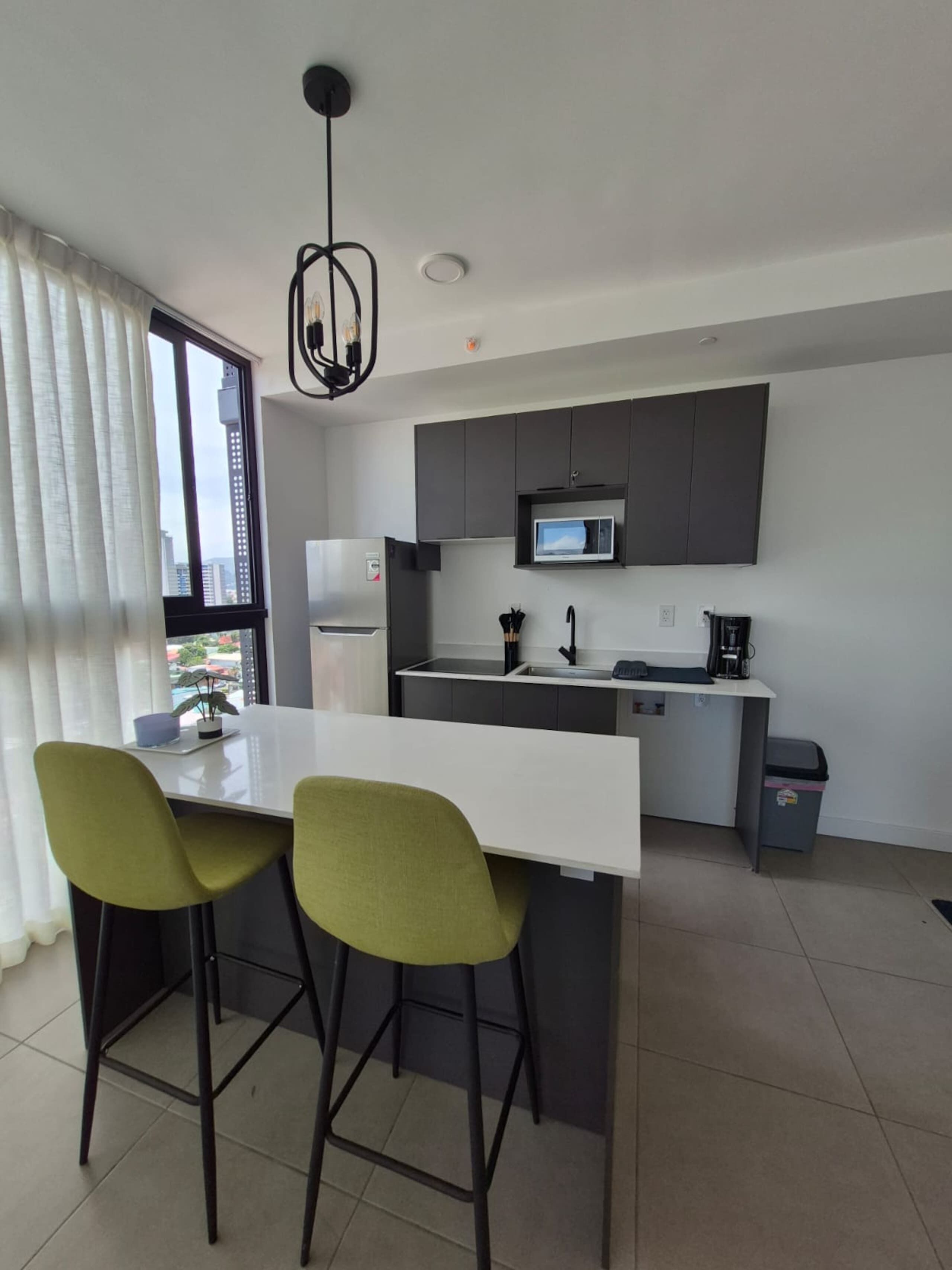 A modern kitchen with a white countertop, two green chairs, a microwave, and a black ceiling light.