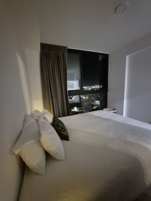 A hotel room with a bed, a window with curtains, and a view of a cityscape at night. - Liva Escalante Sky Retreat | Panoramic City Views & Walking Distance to Restaurants (San José)