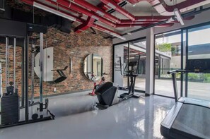 Ein Fitnessraum mit Trainingsgeräten, einer Ziegelwand und großen Fenstern.