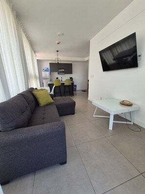 A modern living room with a grey sofa, a small white table, and a flat-screen TV mounted on the wall. - Liva Escalante Sky Retreat | Panoramic City Views & Walking Distance to Restaurants (San José)