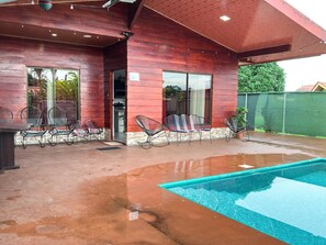 Una casa moderna con piscina, que cuenta con un porche cubierto con sillas y una mesa.