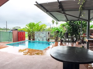 A swimming pool with a tiled deck, surrounded by potted plants and a covered patio area. - 4-bedroom house with AC in La Fortuna (La Fortuna)
