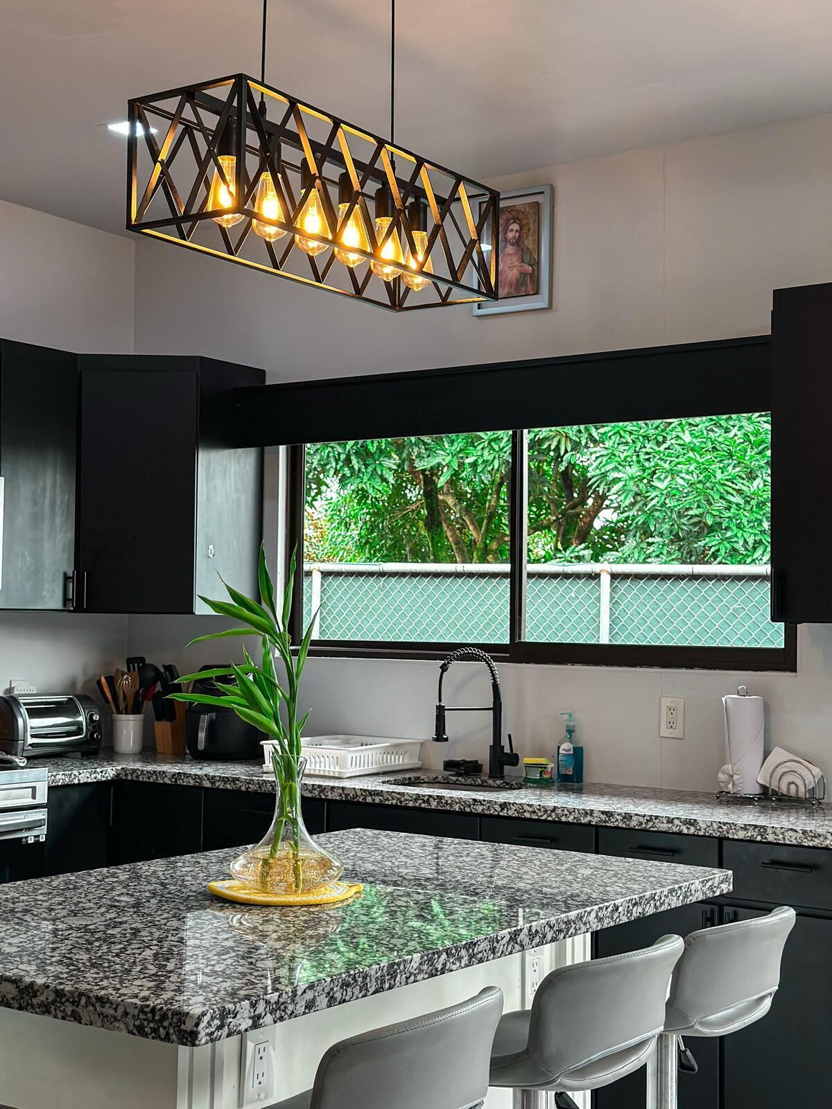 Una cucina moderna con un piano di lavoro in granito, uno schienale bianco e nero, un forno integrato e una finestra con vista sul verde.