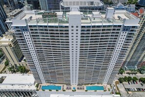 Un hotel modern amb nombroses balconades, piscina i zona d'aparcament.