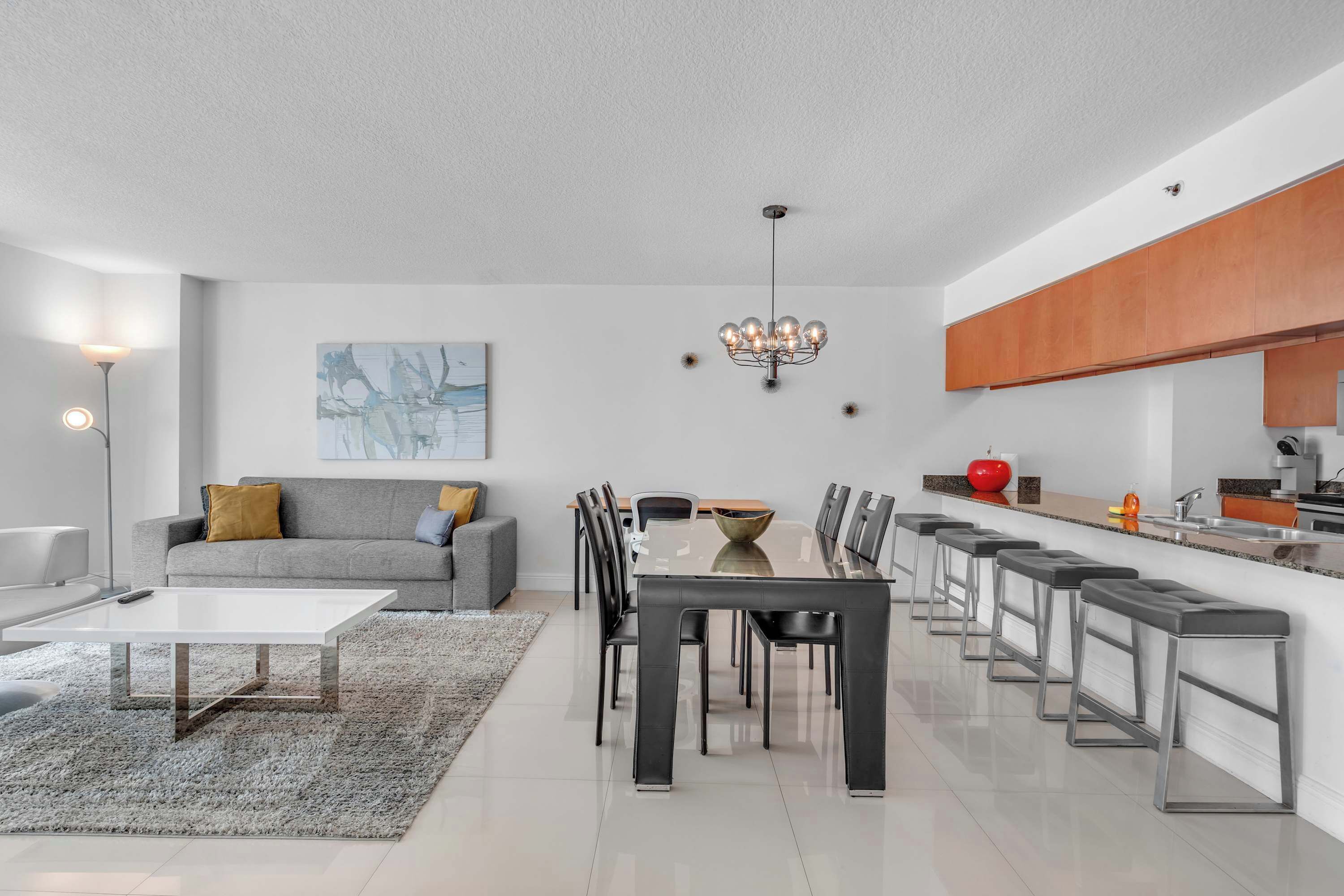 A modern living room with a grey sofa, a coffee table, and a dining area with a glass table and metal chairs.