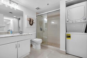 Un bany modern amb un cubicle de dutxa de vidre, un vàter i una safata encastrada per a la rentadora i l'assecadora.