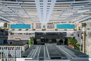 A high-rise building with multiple balconies, two swimming pools, and a parking area. - The Club Brickell | 39th Floor Bay View (Miami)