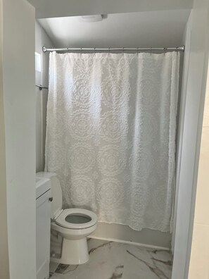 Une salle de bain avec des toilettes, un rideau de douche et un sol en marbre.