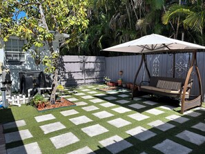 Un jardin avec une pelouse à carreaux, une balançoire et un parasol de patio.