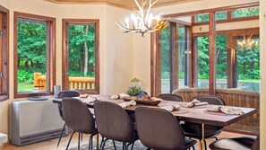 A dining area with a table set for four, surrounded by chairs, with large windows offering a view of greenery outside. - Winter Court by Avantstay Game Room Private Basketball Court Fire Pit Near Skiing & Raceway (Pocono Summit)