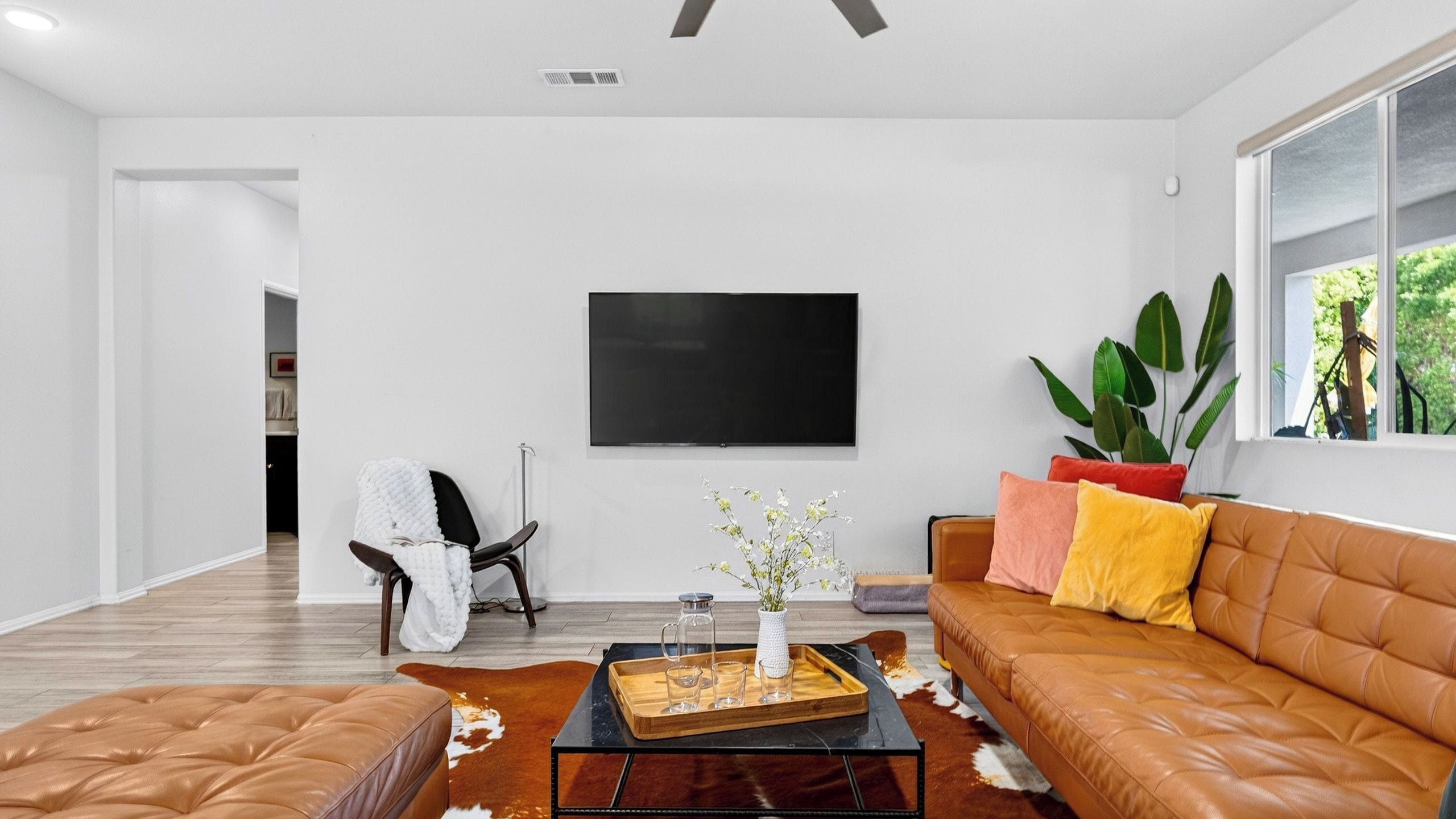 Un salon moderne avec un canapé en cuir, une table basse et un téléviseur à écran plat fixé au mur.