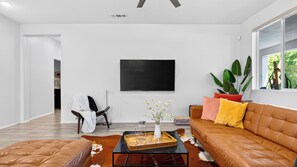 A modern living room with a leather sofa, a coffee table, and a flat-screen TV mounted on the wall. - The Encore by Avantstay Pool + Hot Tub + Outdoor Pool Table + Fire Pit Mins to the Polo Fields (Indio)