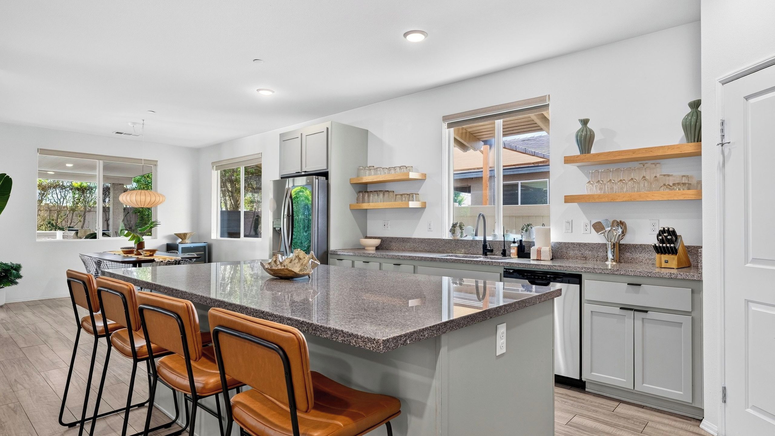 A modern kitchen with a central island, bar stools, and a view of the outdoors.