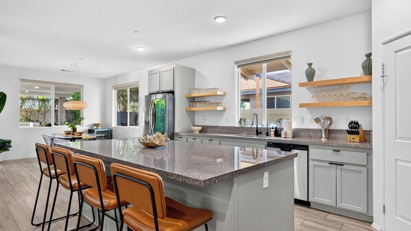 A modern kitchen with a central island, bar stools, and a view of the outdoors. - The Encore by Avantstay Pool + Hot Tub + Outdoor Pool Table + Fire Pit Mins to the Polo Fields (Indio)