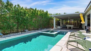 Une piscine avec un espace patio, entourée d’arbres et dotée d’un coin salon abrité.