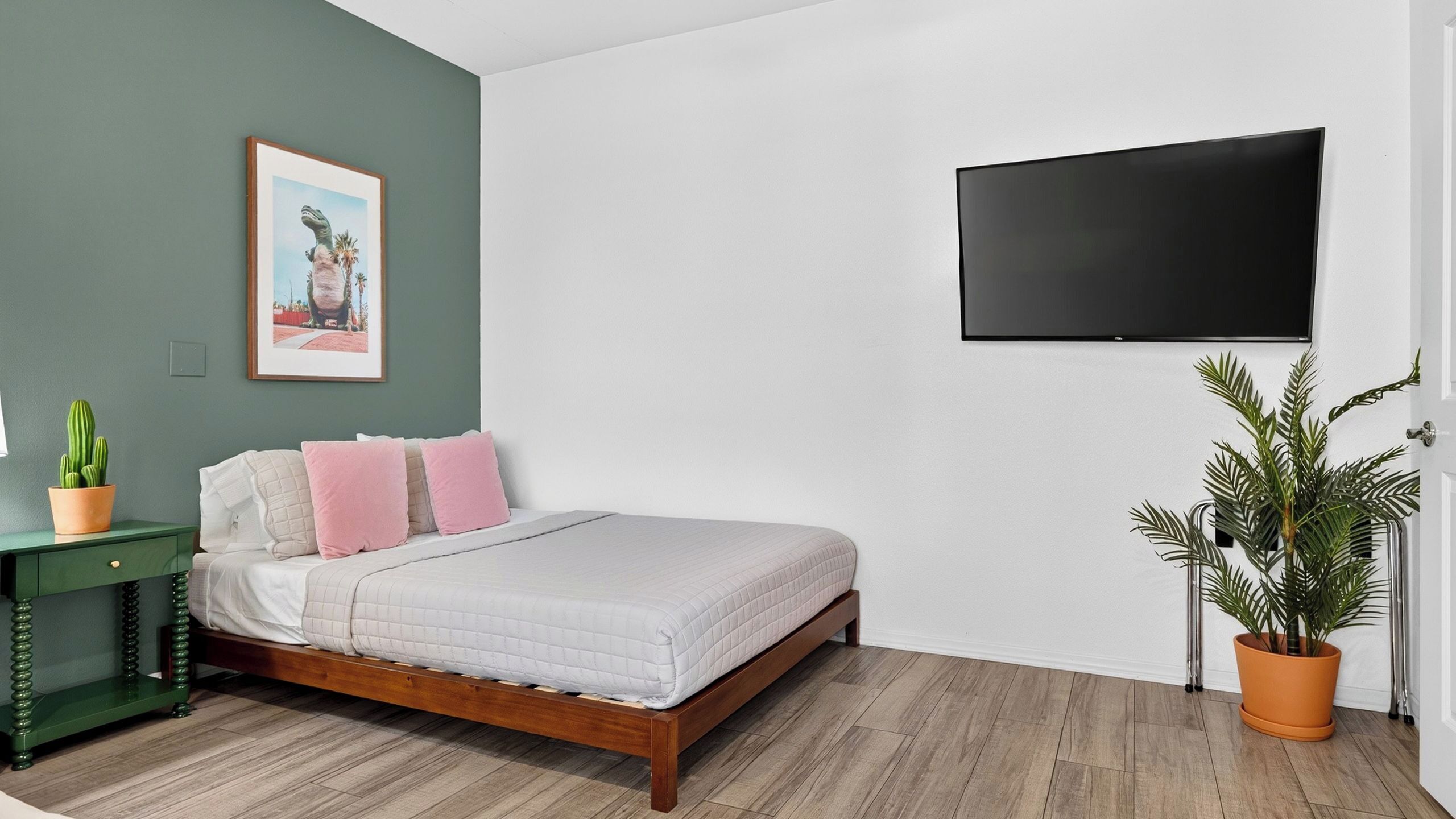 A bedroom with a bed, a green nightstand, a potted plant, and a wall-mounted TV.
