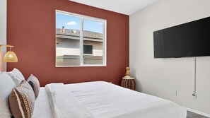 Ein Schlafzimmer mit Bett, Fenster, Fernseher und Lampe.