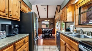 A kitchen with wooden cabinets, a refrigerator, a coffee maker, and a dishwasher. - Dancing Bear by Avantstay Cozy Cabin + Hot Tub + Decks Arcade + Mountain Views Near Park (Sevierville)