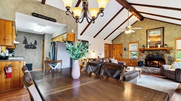A spacious living room with a fireplace, a dining area with a large wooden table, and a kitchen with wooden cabinets.