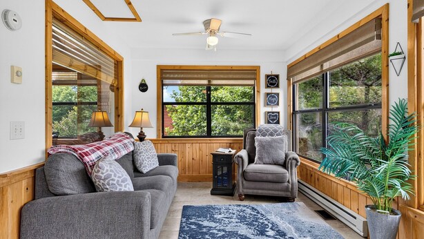 A cozy living room with a sofa, armchair, and a large window with a view of greenery. - Dancing Bear by Avantstay Cozy Cabin + Hot Tub + Decks Arcade + Mountain Views Near Park (Sevierville)