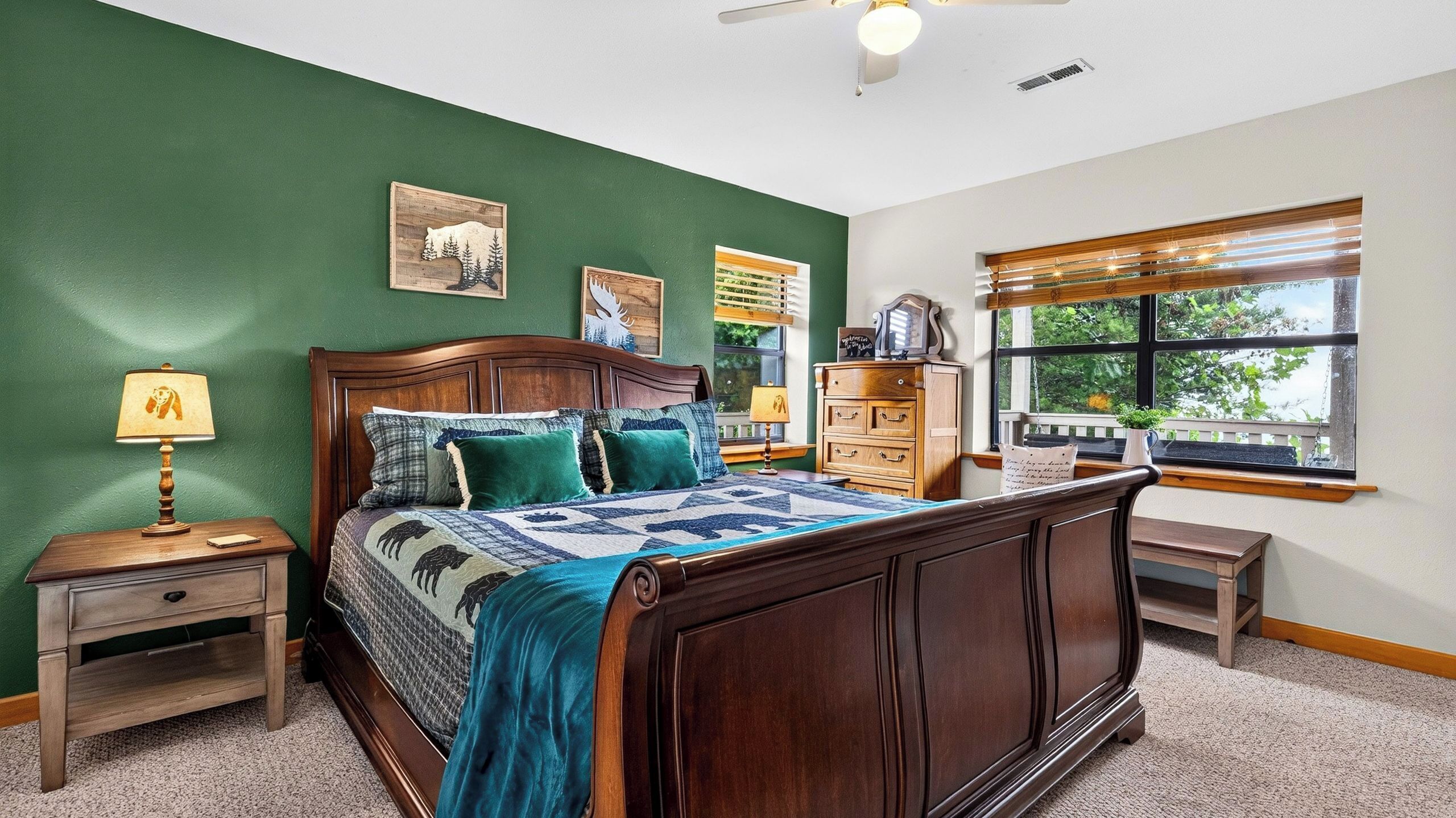 A bedroom with a wooden bed, green walls, a window with a view, and a nightstand with a lamp.