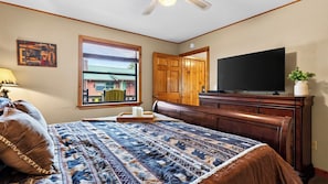 A bedroom with a large bed, a television, a wooden dresser, a window with blinds, and a door. - Dancing Bear by Avantstay Cozy Cabin + Hot Tub + Decks Arcade + Mountain Views Near Park (Sevierville)