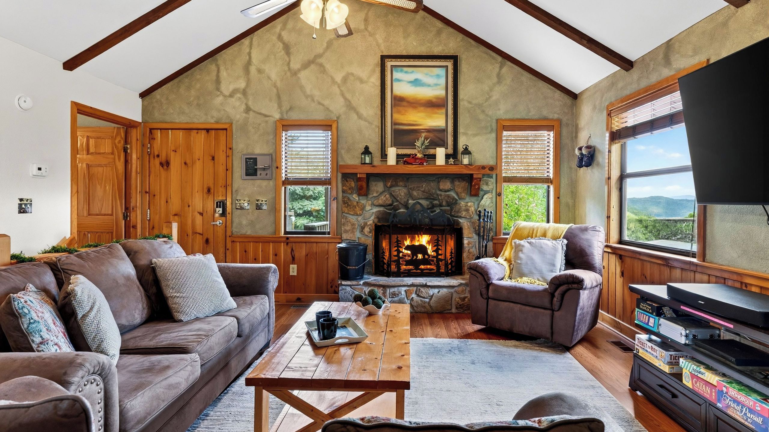 A cozy living room with a fireplace, wooden furniture, and a view of the outdoors.