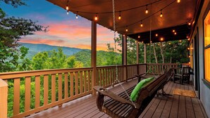 A wooden deck with a swing chair and a bench, overlooking a forested landscape. - Dancing Bear by Avantstay Cozy Cabin + Hot Tub + Decks Arcade + Mountain Views Near Park (Sevierville)