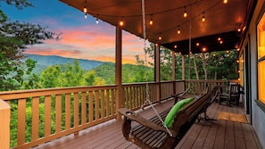A wooden deck with a swing chair and a bench, overlooking a forested landscape. - Dancing Bear by Avantstay Cozy Cabin + Hot Tub + Decks Arcade + Mountain Views Near Park (Sevierville)