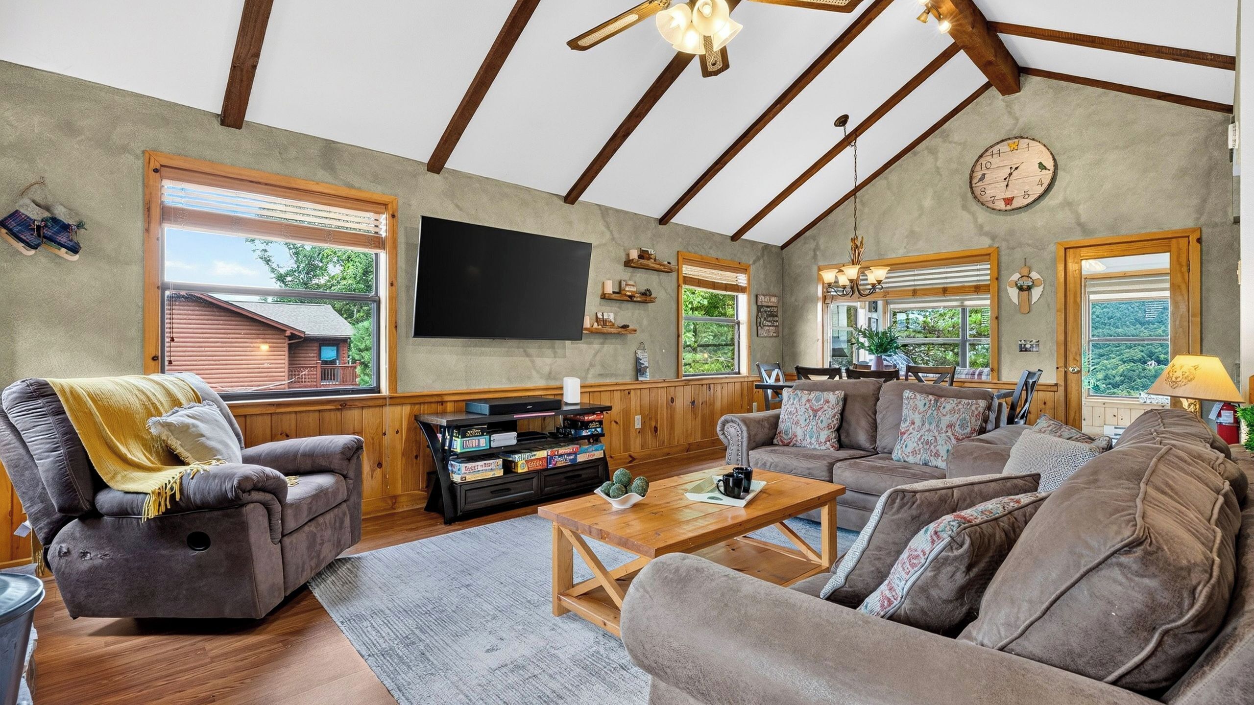 A spacious living room with a large flat-screen TV, wooden furniture, and a view of the outdoors.