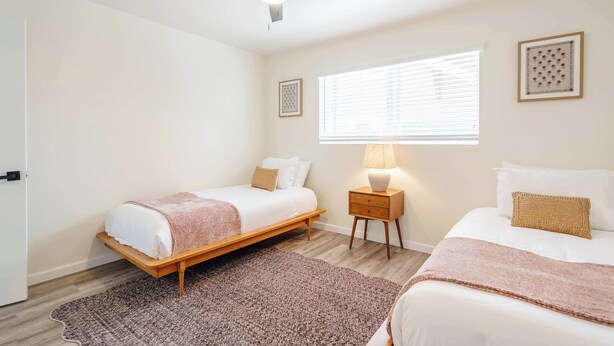 Ein Schlafzimmer mit zwei Betten, einem Deckenventilator, einem Nachttisch mit Lampe und einem Fenster mit Jalousien.