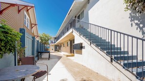 Ein Wohngebäude mit einer Treppe zu einer oberen Ebene, einer kleinen Außenbereich-Sitzgelegenheit mit Tisch und Stühlen sowie einem eingezäunten Garten.