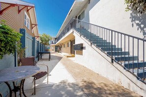 Ein Wohngebäude mit einer Treppe zu einer oberen Ebene, einer kleinen Außenbereich-Sitzgelegenheit mit Tisch und Stühlen sowie einem eingezäunten Garten.