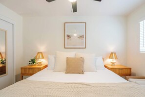 Un dormitorio con una cama, dos mesitas de noche, lámparas, un cuadro en la pared y una ventana con persianas.