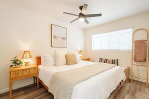 A bedroom with a bed, bedside lamps, a ceiling fan, a window with blinds, and a towel rack. - Coastal 2BR | Walk to Ocean Beach & Cafés (San Diego)