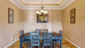 A dining room with a wooden table and chairs, a chandelier, and two framed pictures on the walls. - Graceland by Avantstay Private Pool + Spa + Fenced Backyard Near North Padre Island (Corpus Christi)