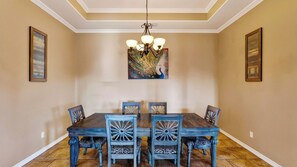 A dining room with a wooden table and chairs, a chandelier, and two framed pictures on the walls. - Graceland by Avantstay Private Pool + Spa + Fenced Backyard Near North Padre Island (Corpus Christi)